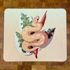 A mousepad decorated with an illustration of a yellow and peach colored ball python snake, known as a banana ball, in front of a plant on a peach background.