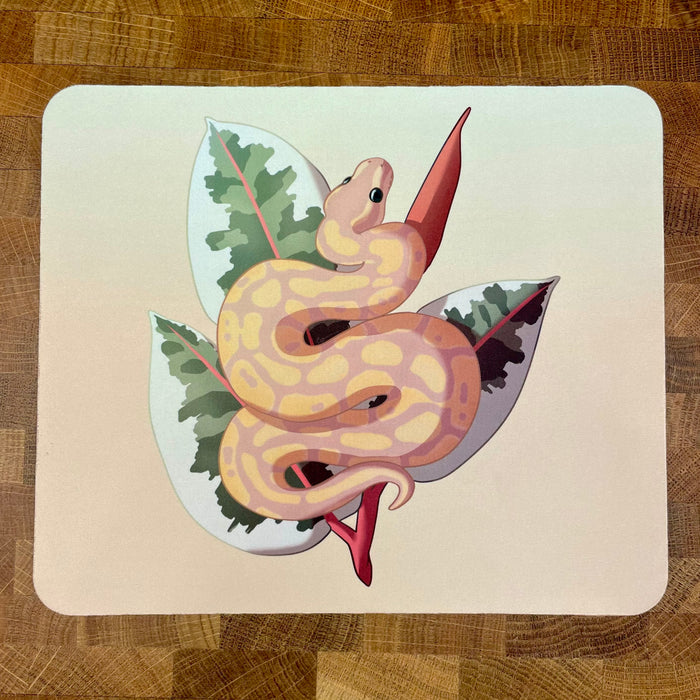 A mousepad decorated with an illustration of a yellow and peach colored ball python snake, known as a banana ball, in front of a plant on a peach background.
