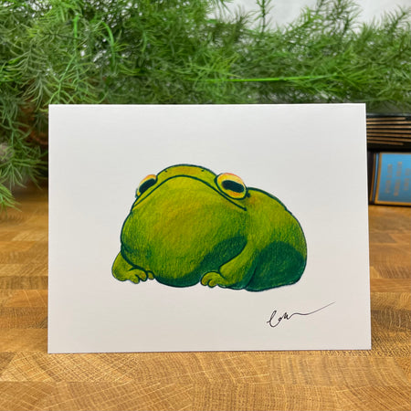 A fun, cartoon illustration of a green frog on a white card, signed by the artist. The inside is not shown but it is blank.