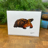 Card with a turtle illustration packaged in clear bag with a white envelope, on a wooden surface with greenery in the background