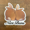 Sticker of two rabbits with 'Nice Buns' text photographed on a wooden background