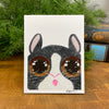 Card with a stylized bunny illustration on a wooden surface with greenery in the background