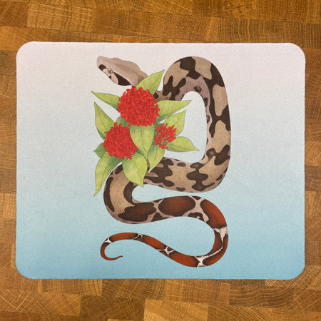 A mousepad decorated with an illustration of a Suriname red-tailed boa constrictor snake with a red flower on a light blue background.
