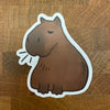 sticker of a cartoon illustration of a sitting capybara photographed on wood background