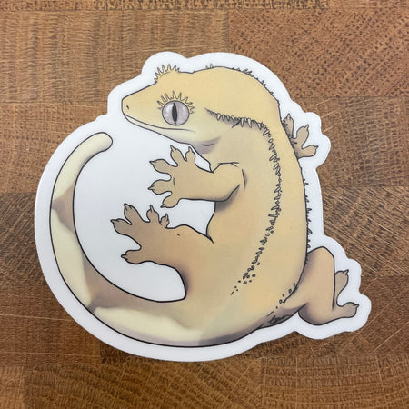 Sticker of a beige crested gecko photographed on a wooden surface