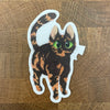 Die cut sticker of a tortoiseshell cat with green eyes photographed on a wooden surface