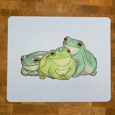 A mousepad decorated with an illustration of three green tree frogs on a light blue background.