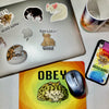 A laptop with stickers on it nest to a mousepad, a phone case, and a mug