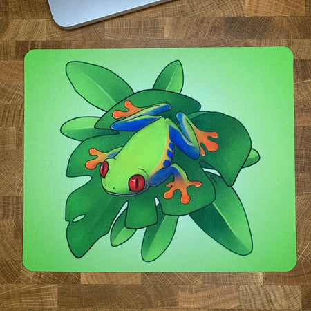 Colorful mousepad with an illustration of a red-eyed tree frog sitting on a green plant.