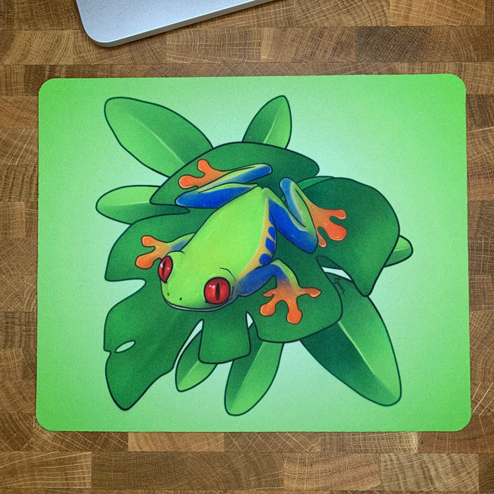 Colorful mousepad with an illustration of a red-eyed tree frog sitting on a green plant.